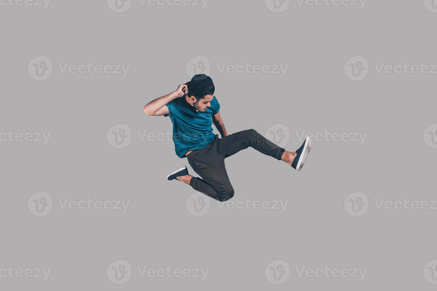 Cool and free. Mid-air shot of handsome young man in cap jumping and gesturing against background photo