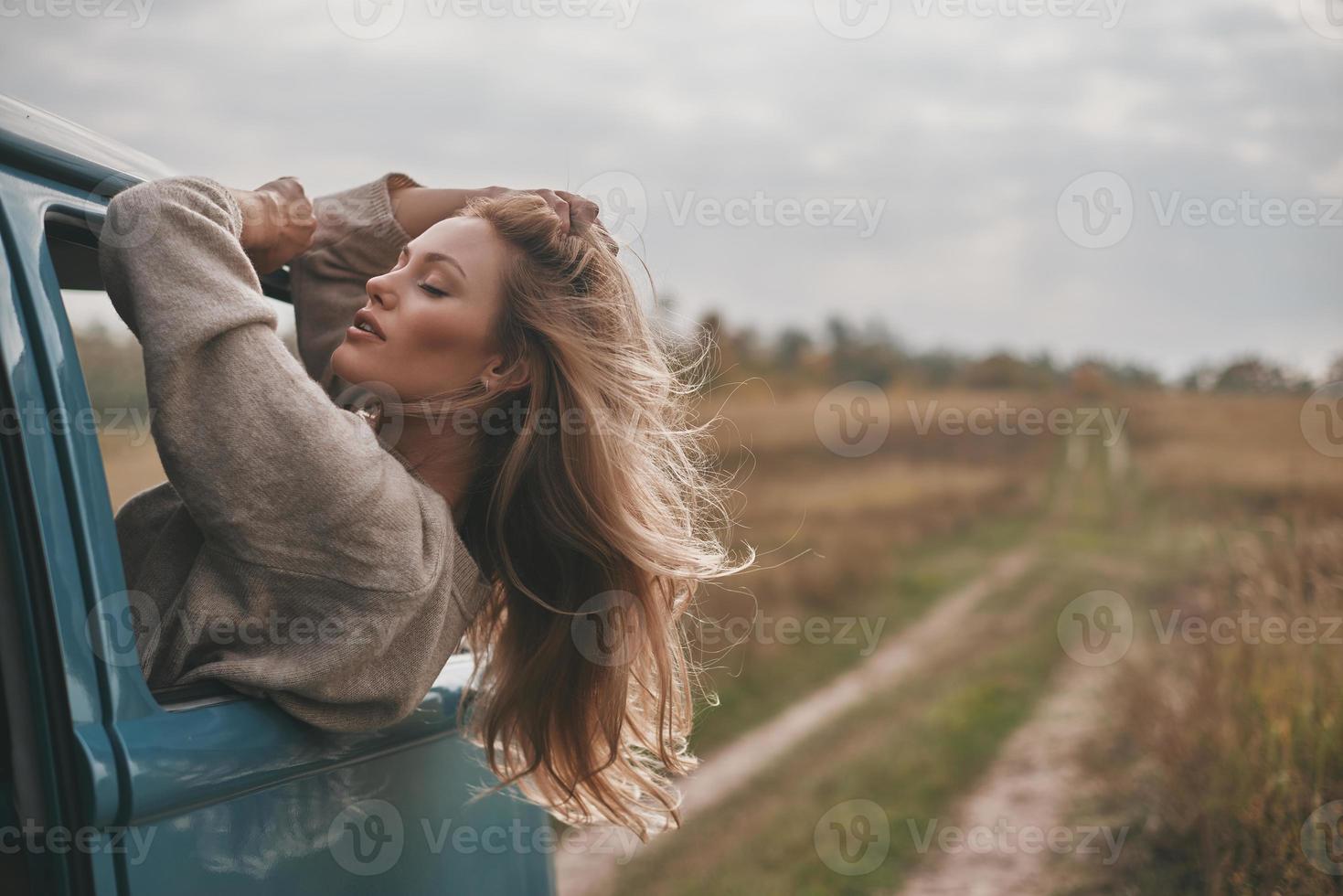 On the way to unknown places. Attractive young woman leaning out the vans window and keeping hand in hair while enjoying the car travel photo