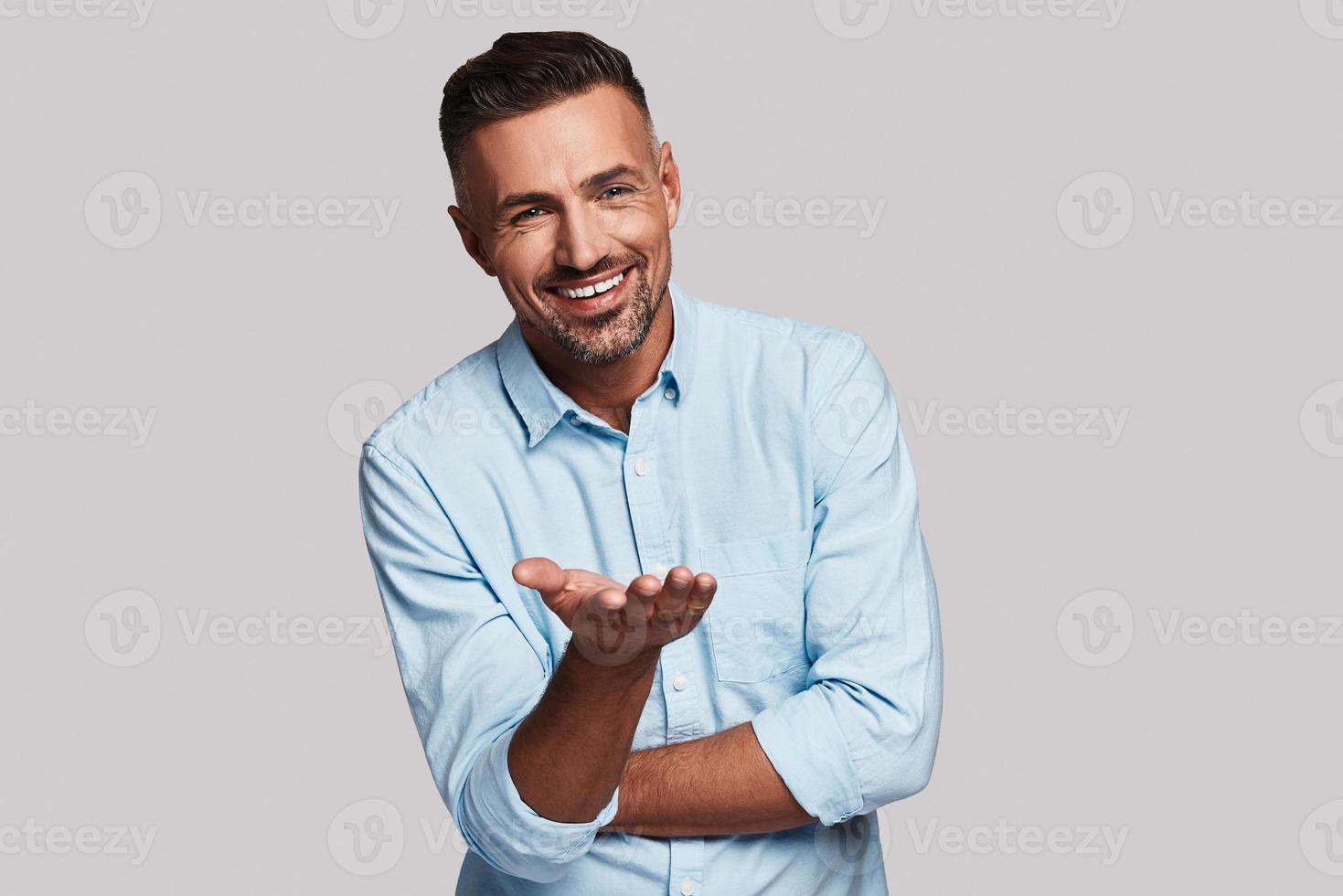 Are you happy Handsome young man smiling and looking at camera while standing against grey background photo