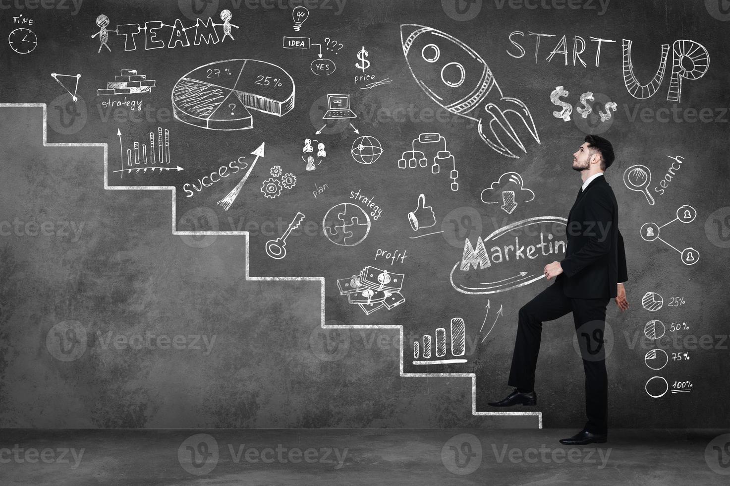 Moving up to success. Full length of confident young man in full suit moving up by illustrated steps and against a concrete wall photo