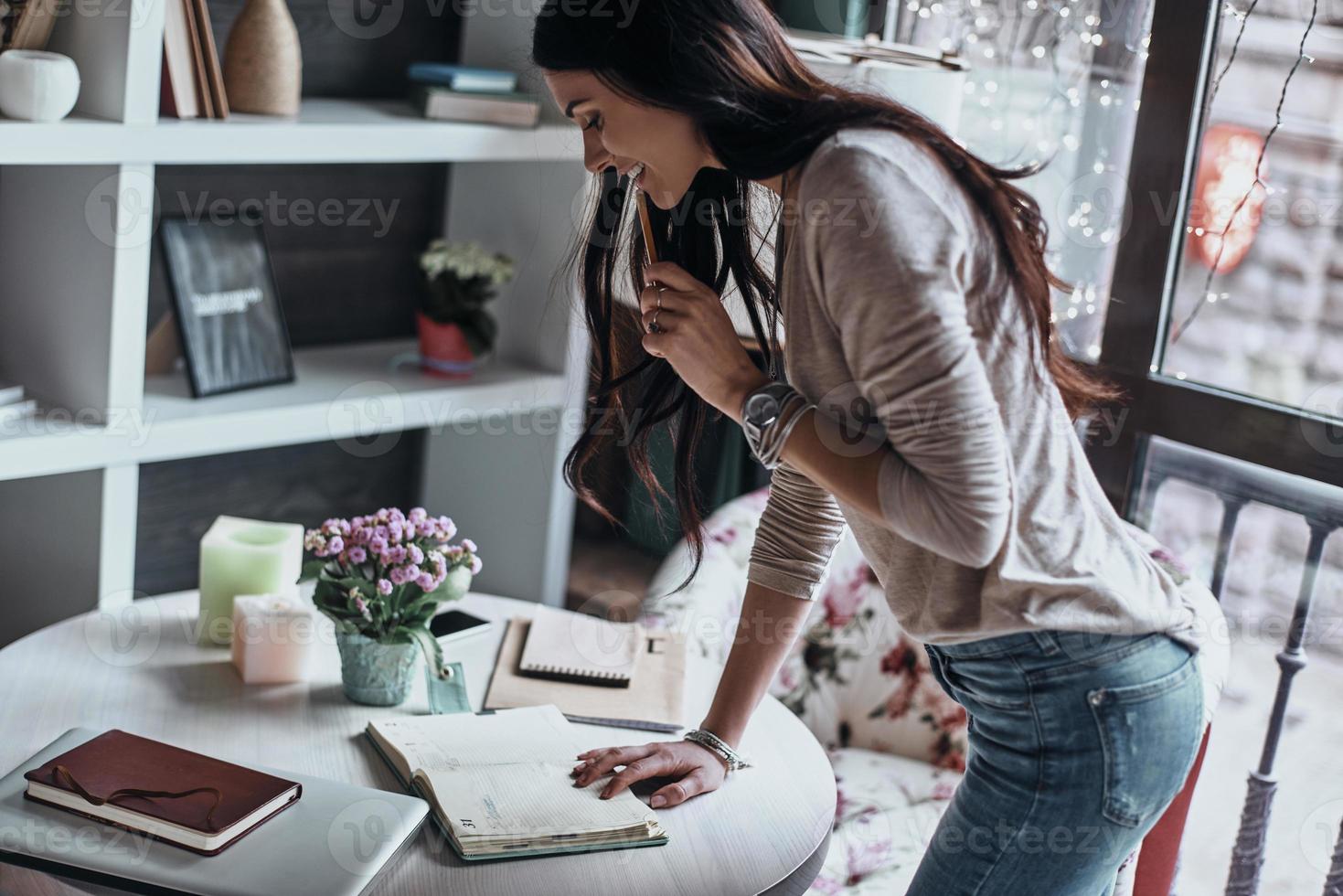 Enyoing nice working day. Beautiful young woman looking in her notebook and touching her lips with pencil while standing in restaurant photo