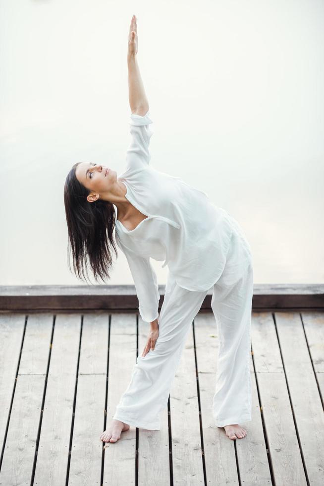 Stretching to the sun. Full length of beautiful young woman in white clothing performing yoga outdoors photo