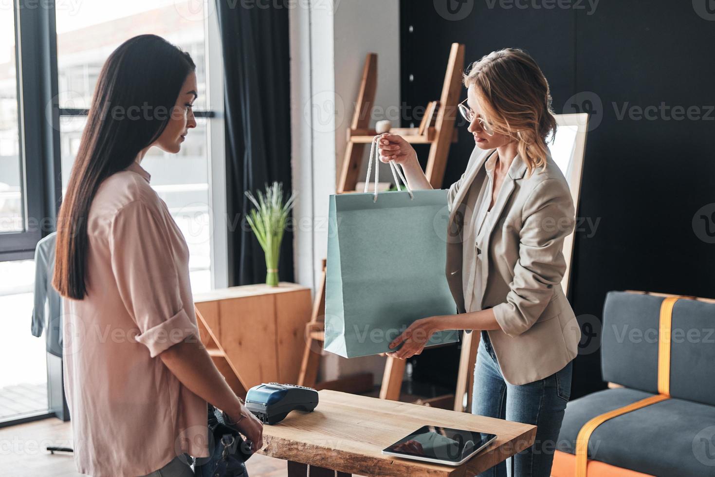 Happy shopping. Beautiful young woman giving a shopping bag to her customer while working in the fashion boutique photo