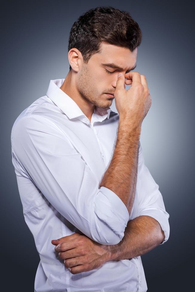 Lost in thoughts. Side view of handsome young man in white shirt holding hand in hair and looking away while standing against grey background photo