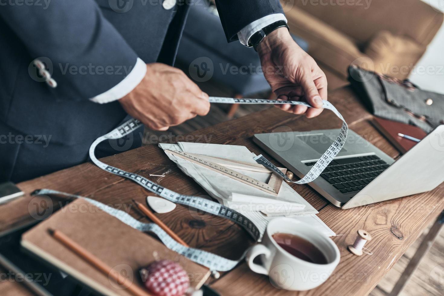 Designing new clothes. Close up top view of fashion designer holding a tape measure while working in clothing design studio photo