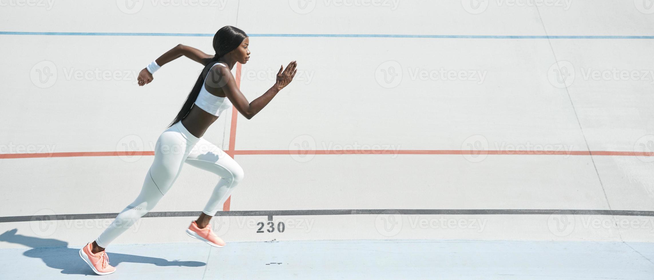 Confident young African woman in sports clothing running on track outdoors photo