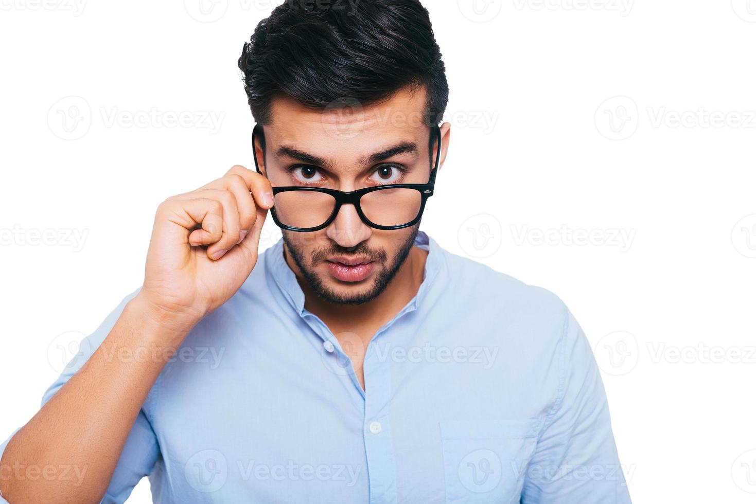 tiene algunos problemas confiado joven indio ajustando sus anteojos y mirando a la cámara mientras está de pie contra el fondo blanco foto