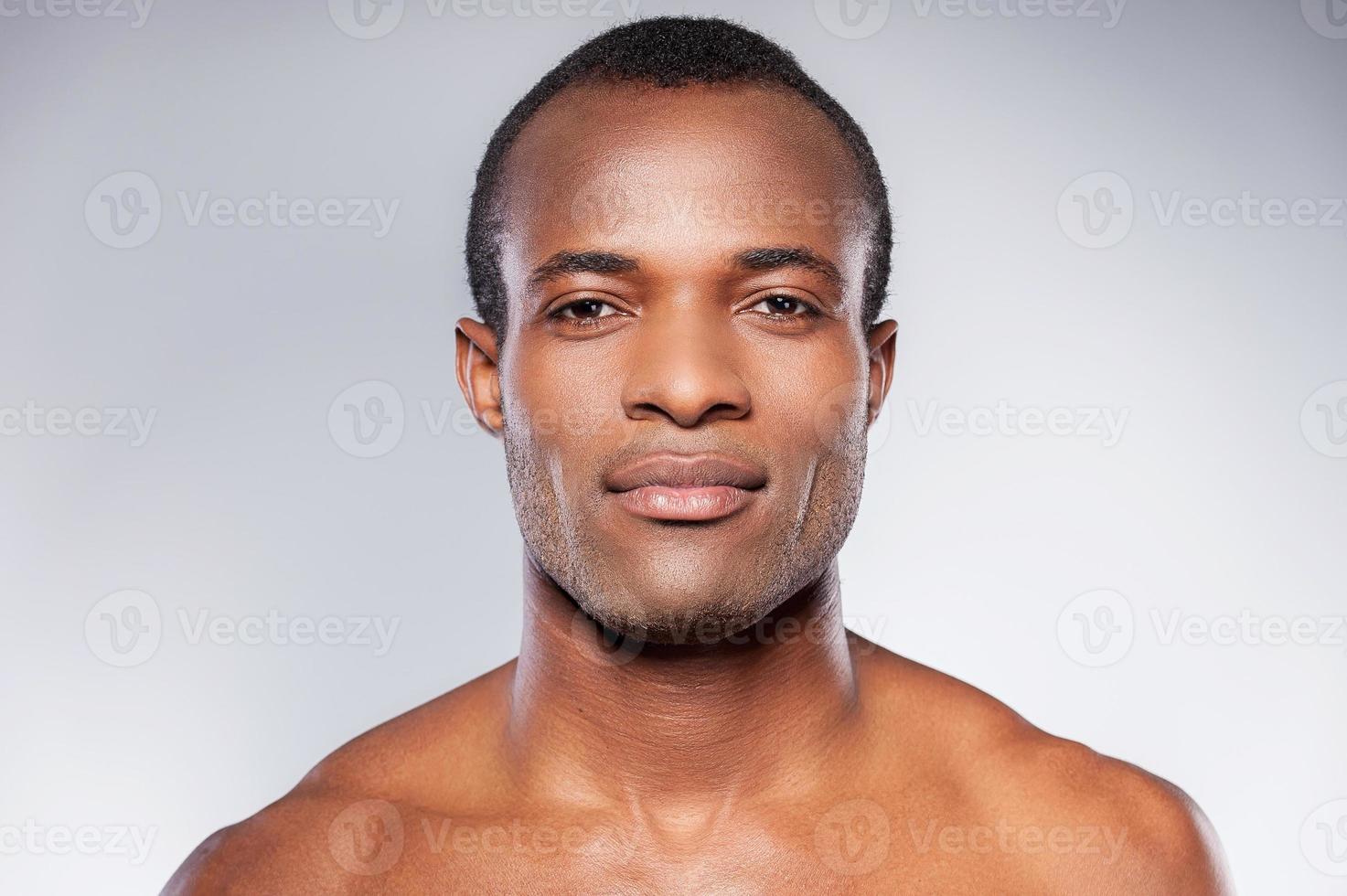 retrato de la masculinidad. retrato de un joven africano sin camisa mirando a la cámara mientras se enfrenta a un fondo gris foto