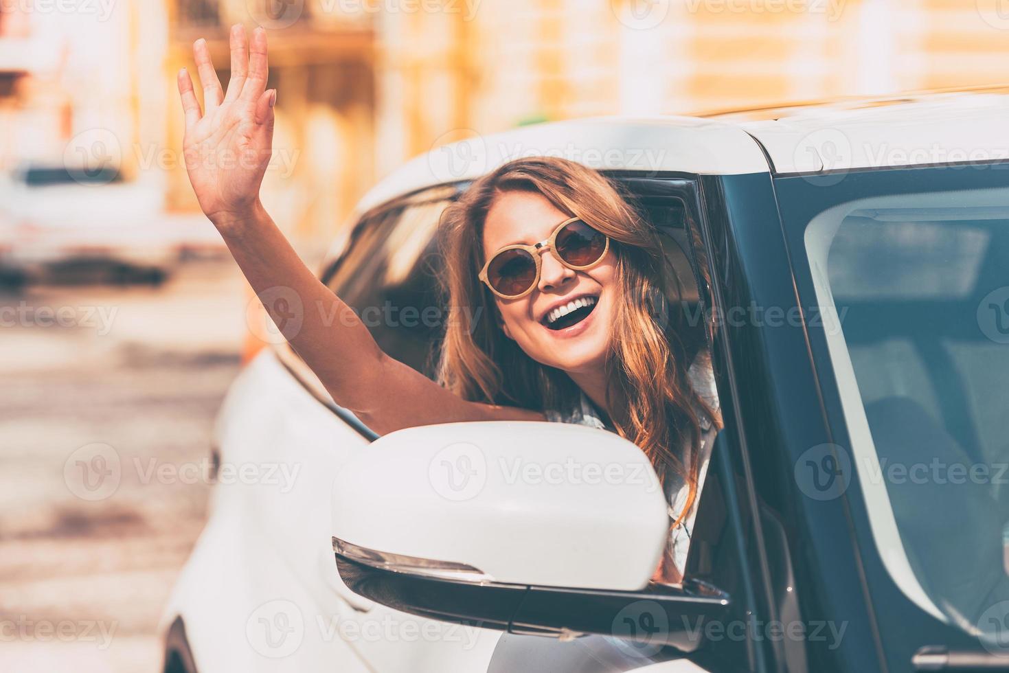 hola hermosas jóvenes mujeres alegres mirando a la cámara con una sonrisa y saludando mientras están sentadas en su auto foto