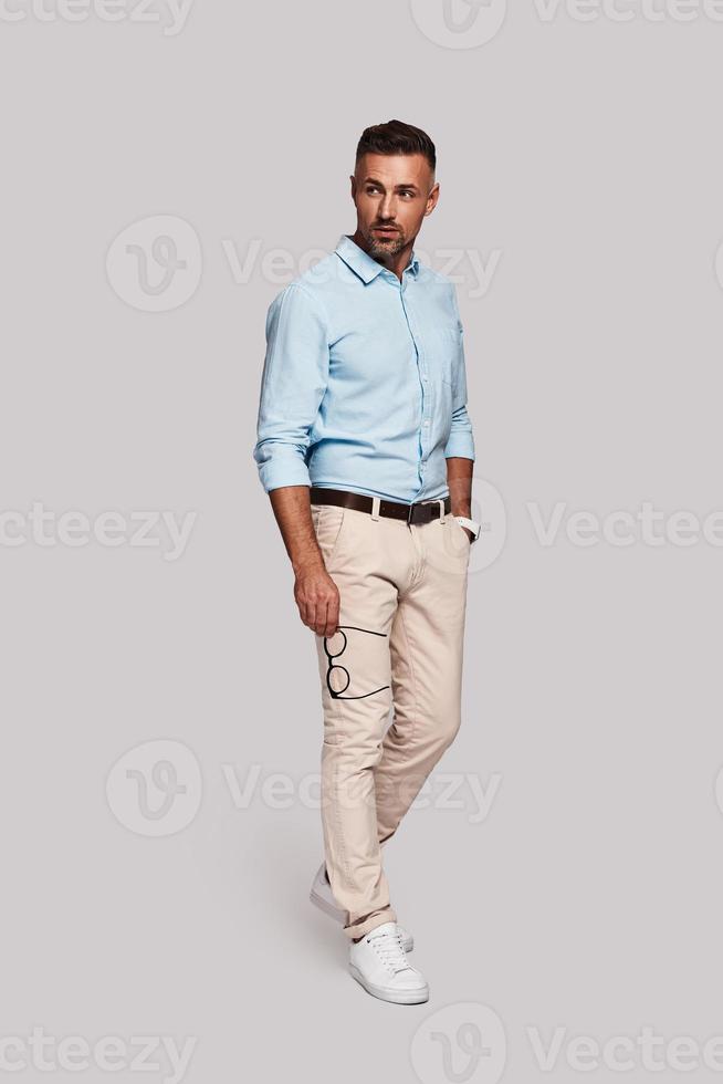 Male beauty. Full length of handsome young man smiling and keeping hand in pocket while walking against grey background photo