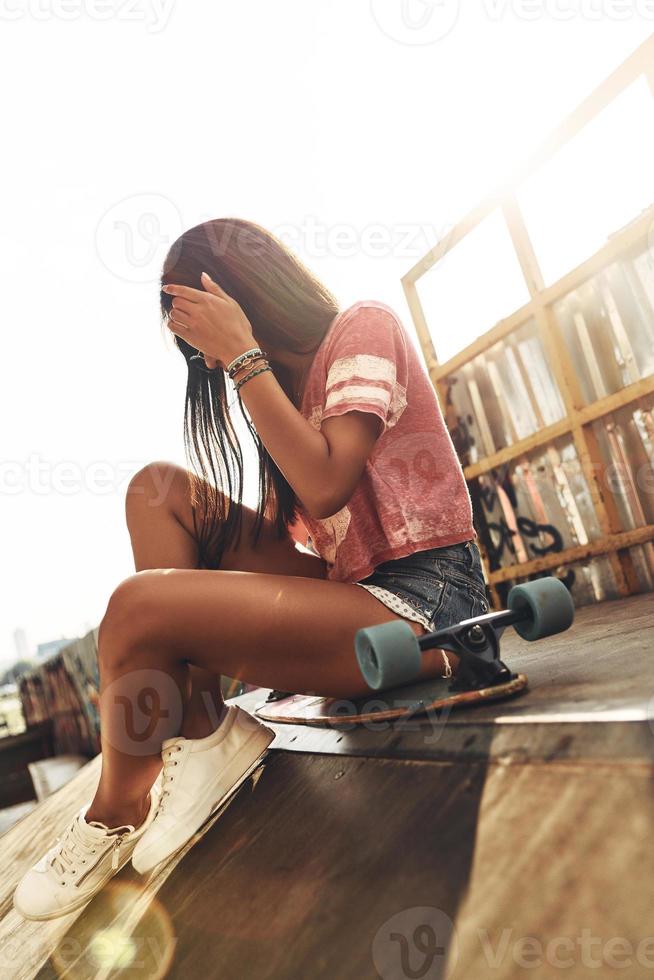 Born to be a skater girl. Attractive young woman adjusting her hair while sitting on the skateboard at the skate park outdoors photo