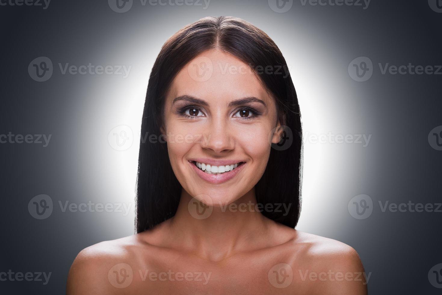 Cheerful beauty. Portrait of smiling young shirtless woman looking at camera while standing against grey background photo