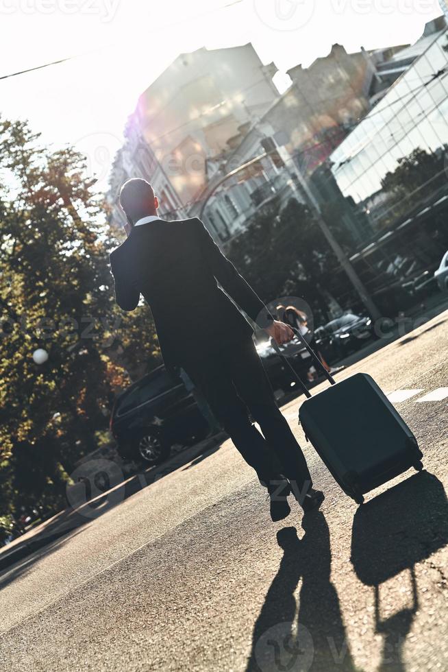 I will be there in time Full length rear view of young man in full suit talking on the phone while walking outdoors photo