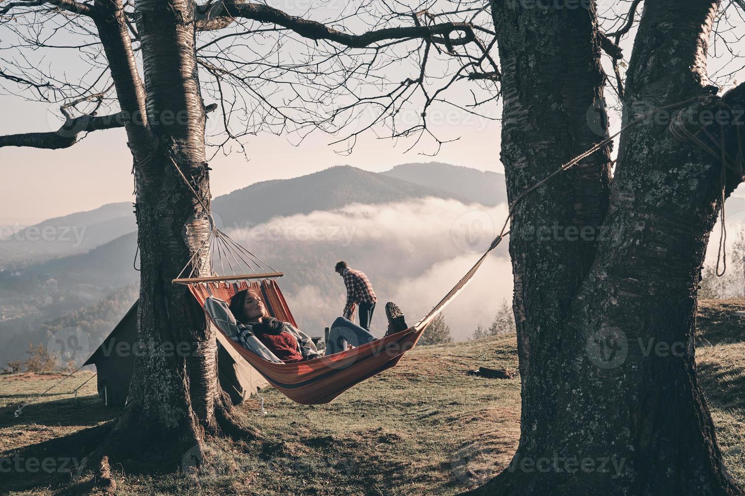 Attractive young woman lying in hammock while camping with her boyfriend photo