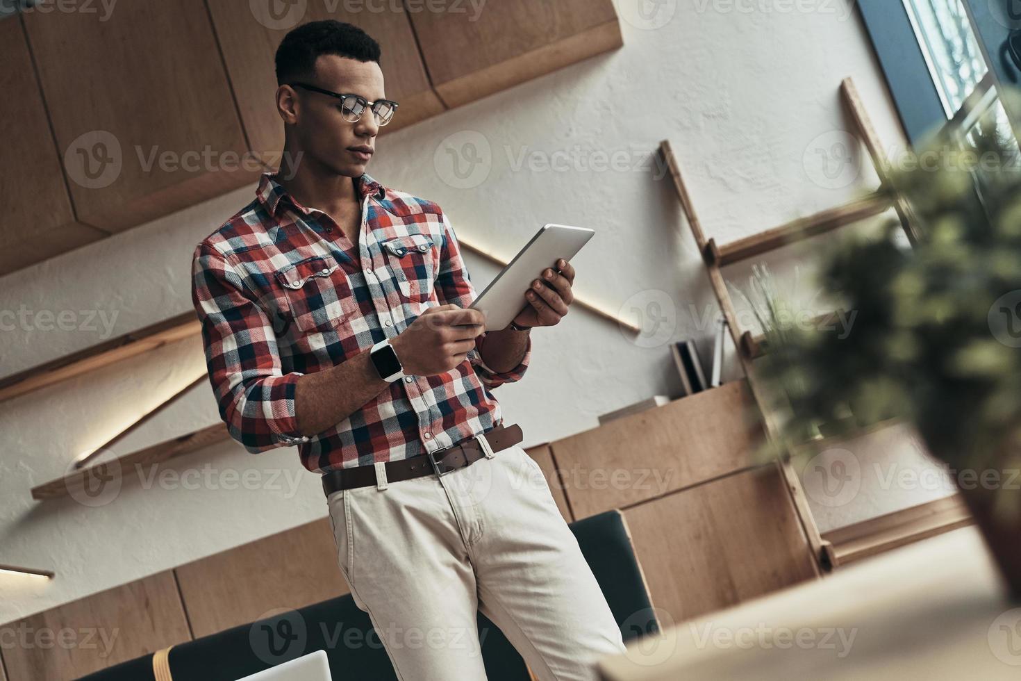 Achieving best results. Handsome young man using digital tablet while standing in the creative working space photo