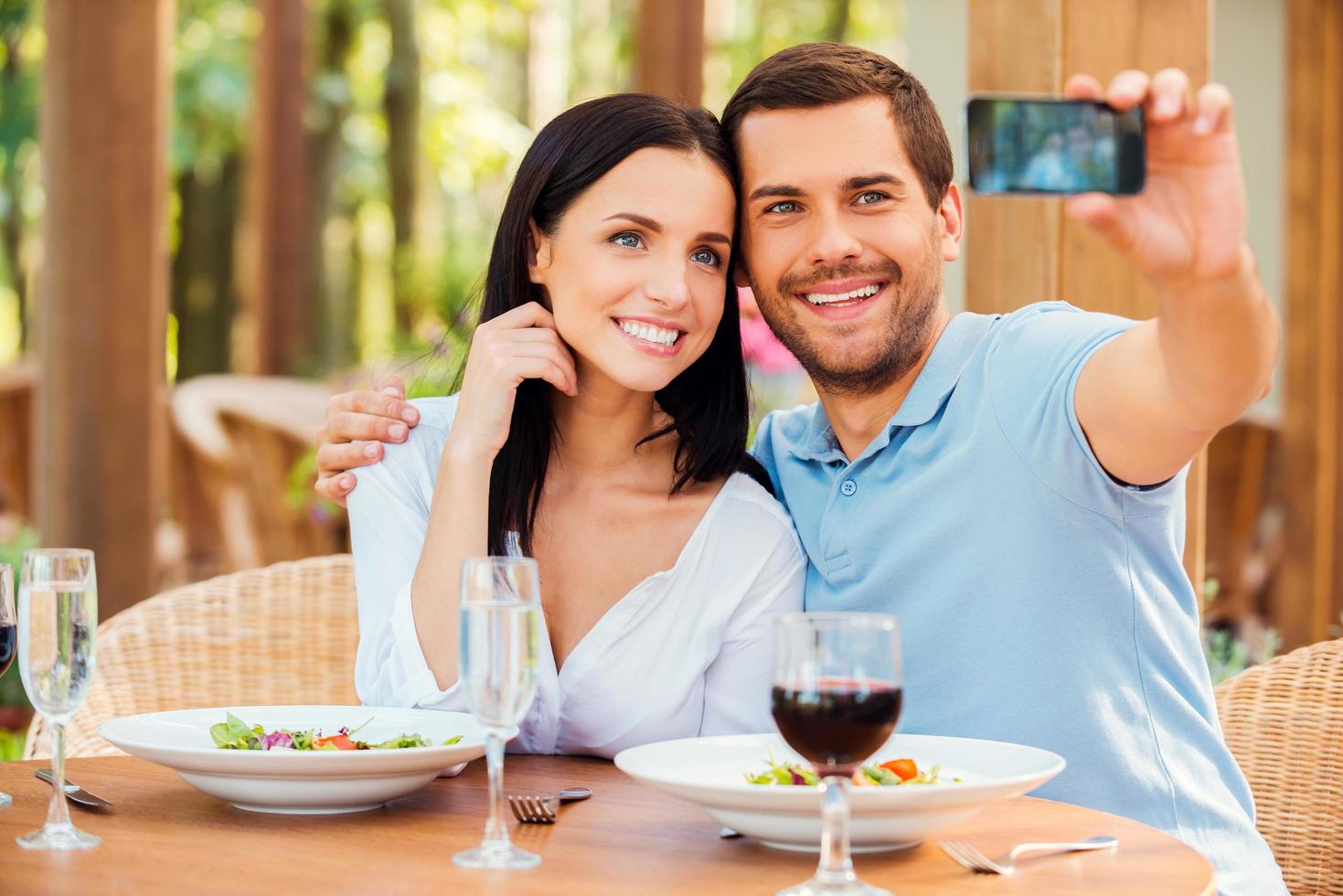 haciendo selfie en restaurante. hermosa joven pareja amorosa haciendo selfie con teléfono móvil y sonriendo mientras se relaja en un restaurante al aire libre juntos foto