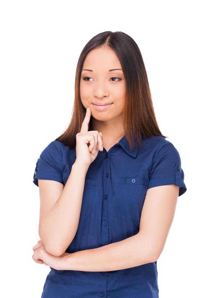 Day dreaming beauty. Beautiful young Asian woman holding hand on chin and looking away while standing isolated on white photo