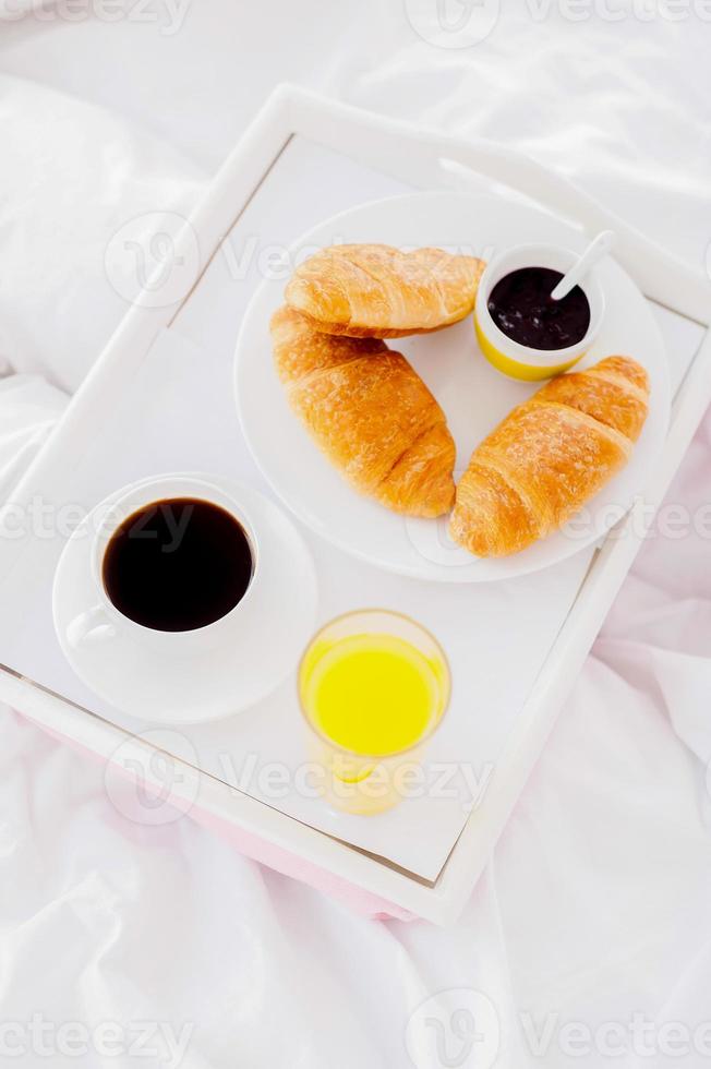 Breakfast in bed. Top view of tray with croissants and drinks laying on bed photo