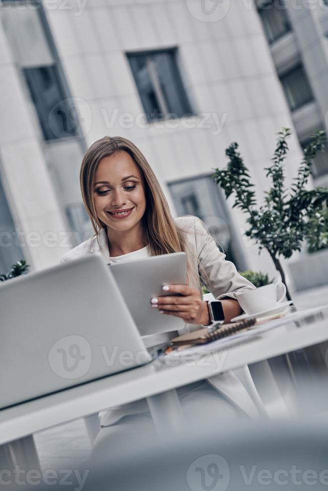 Putting ideas into something real. Beautiful young woman using digital tablet and smiling while sitting in the modern restaurant photo