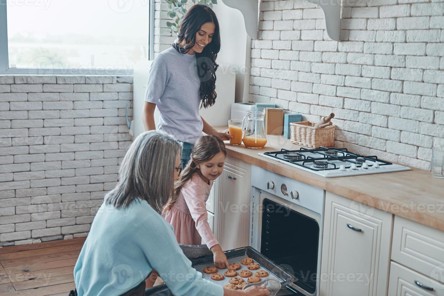 hermosa abuela sacando galletas del horno y sonriendo mientras pasa tiempo con la familia foto