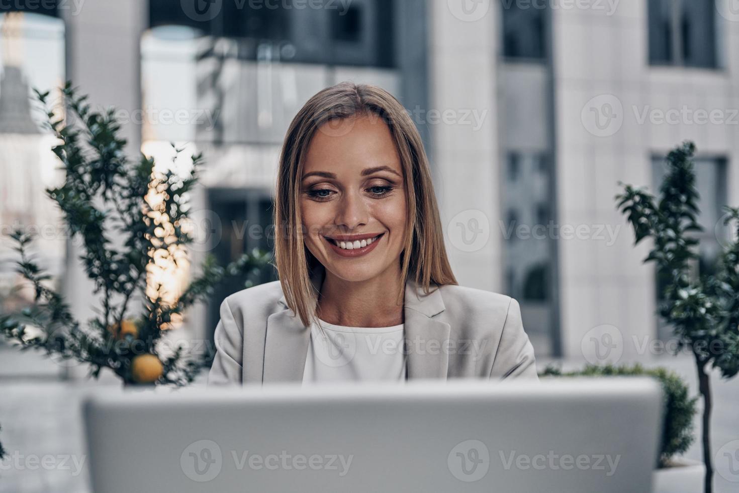 Full concentration at work. Beautiful young woman using laptop and smiling while working indoors photo