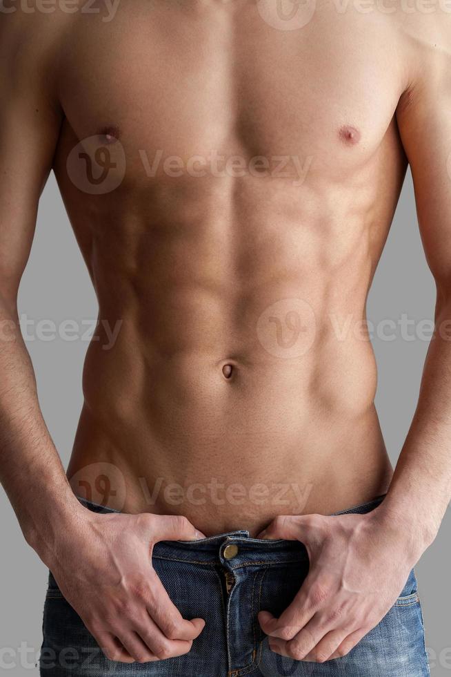 Chiseled chest and abs. Cropped image of muscular man standing isolated on grey background photo