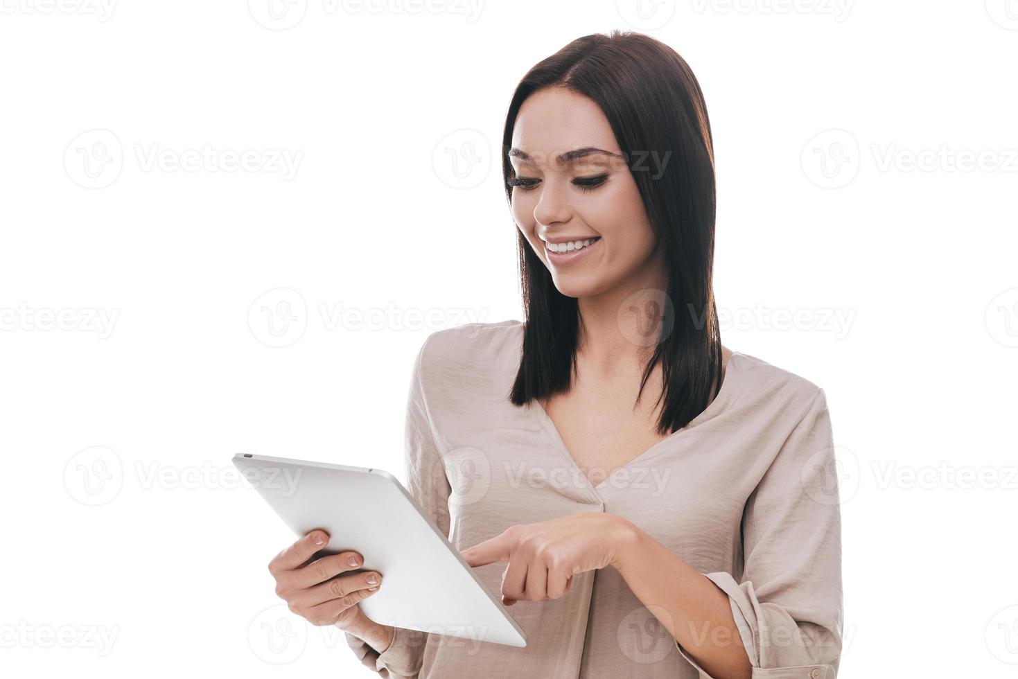 Technologies making life easier. Confident young woman in smart casual wear holding digital tablet and looking at it with smile while standing against white background photo