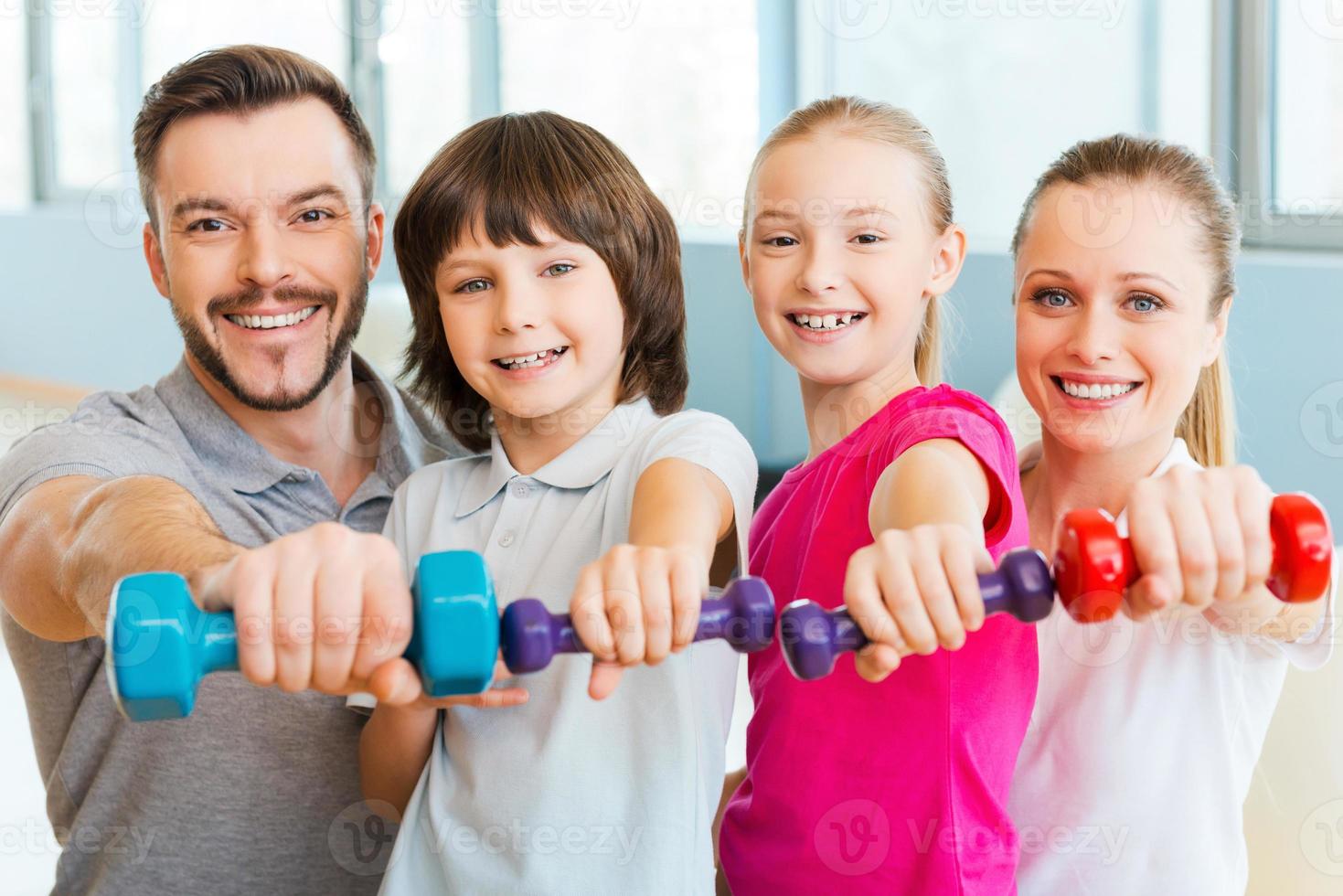 Living a healthy life together. Happy family holding different sports equipment while standing close to each other in health club photo