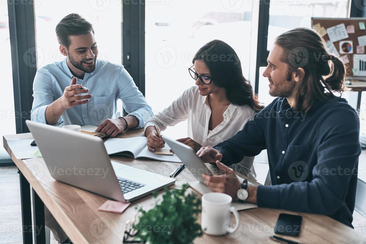 Passionate about their project. Group of young modern people in smart casual wear working together and smiling while sitting in the creative office photo