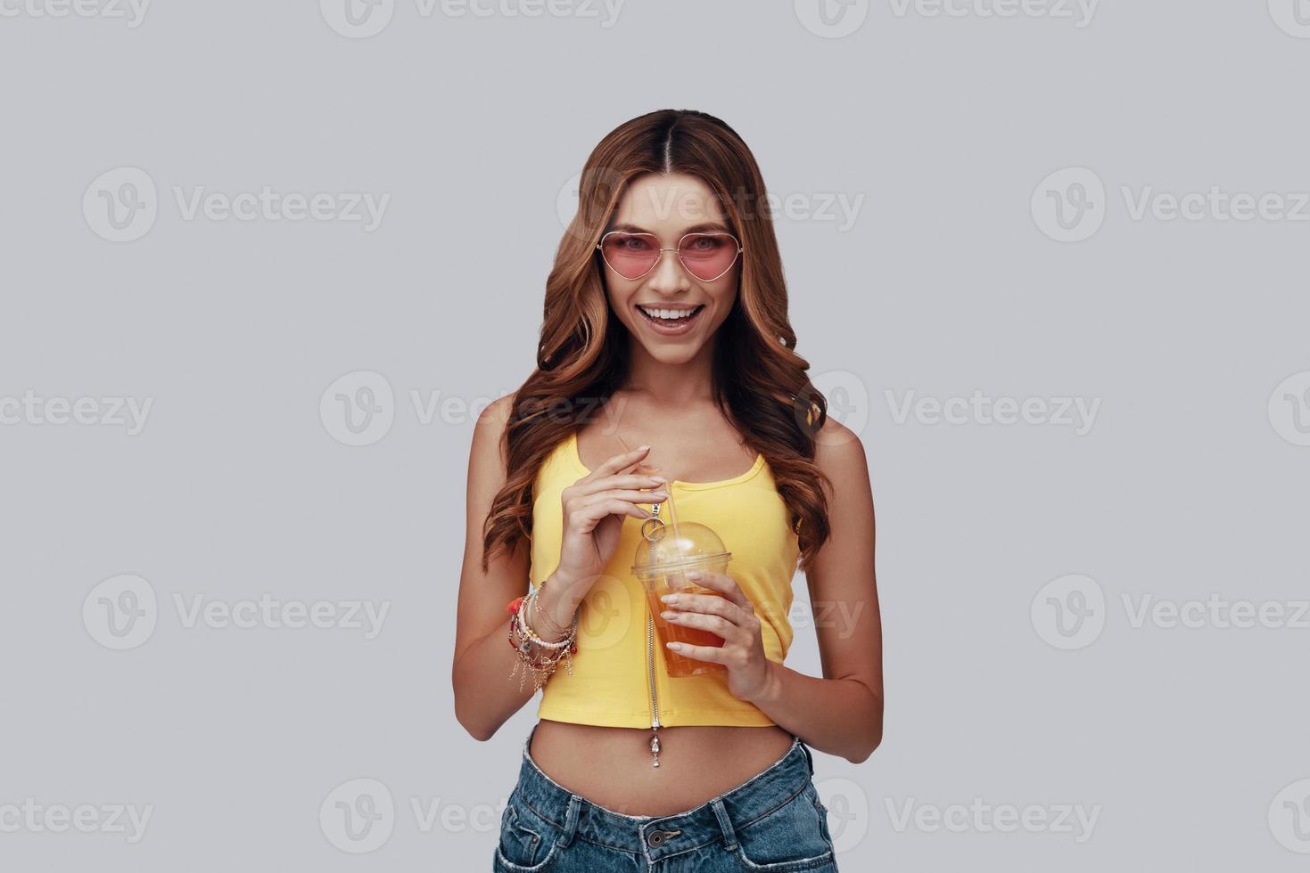 Attractive young woman looking at camera and smiling while standing against grey background photo