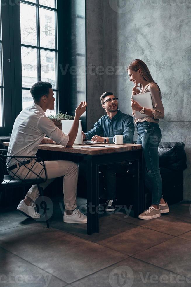 Group of young modern people in smart casual wear discussing something while working in office photo
