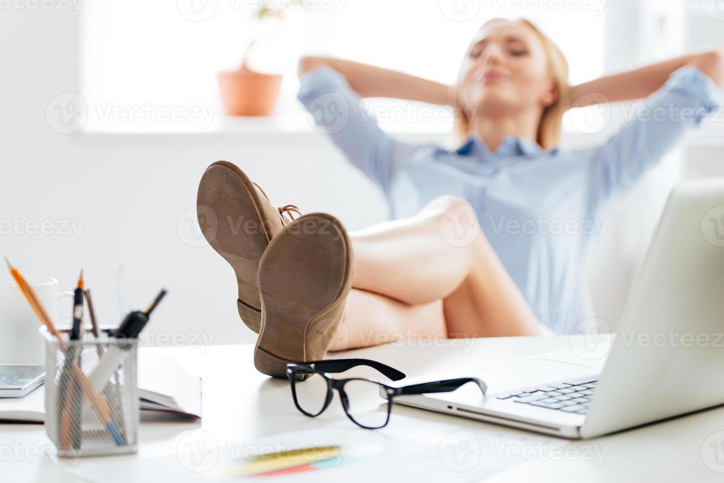 Time for a little brake. Close-up of young beautiful woman holding hands behind her head and keeping legs on table while sitting at her working place photo