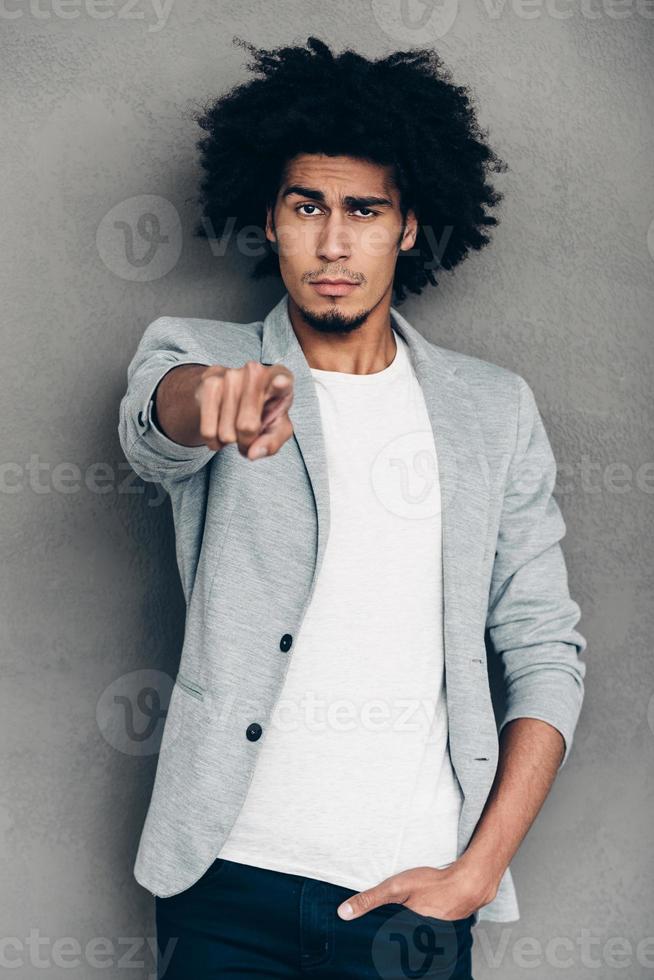 I choose you Young African man pointing on you and looking at camera while standing against grey background photo