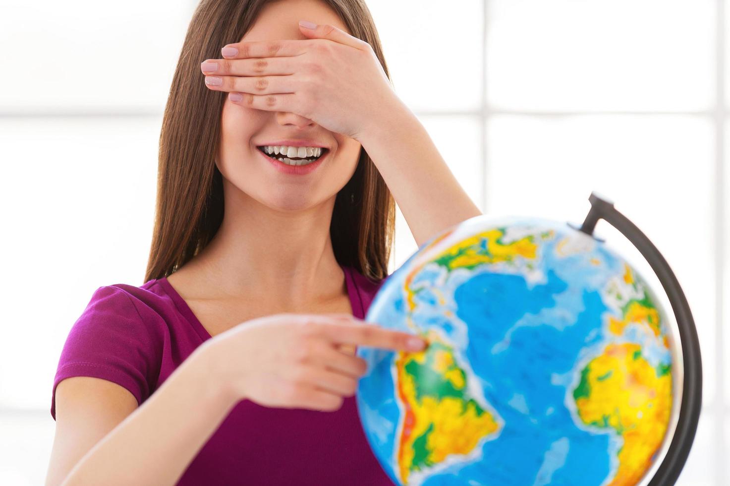 Choosing a traveling point. Cheerful little girl in formalwear examining globe with a loupe while sitting at the table photo