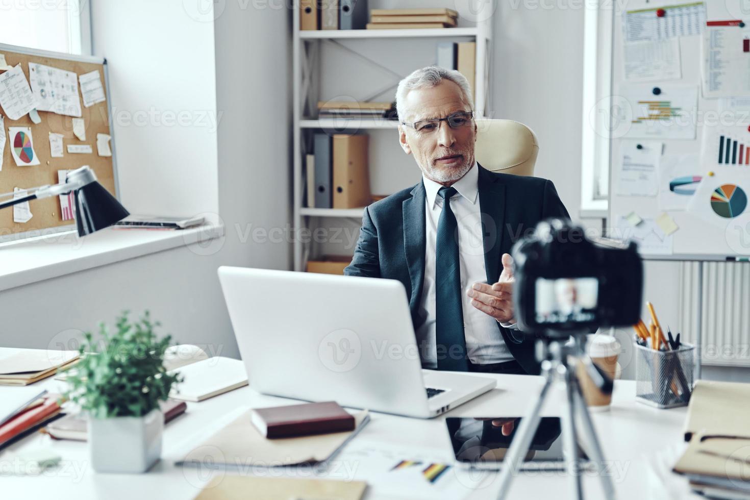 Senior man in elegant shirt and tie working using laptop while making social media video photo