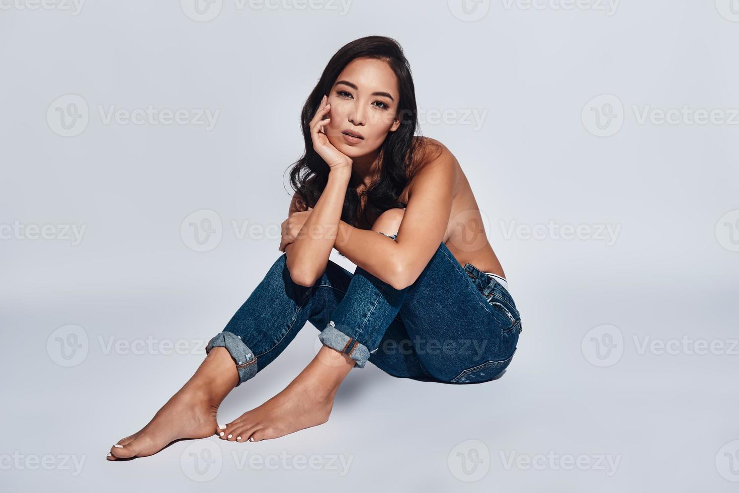 Enjoying her beauty. Attractive young woman looking at camera while sitting against grey background photo