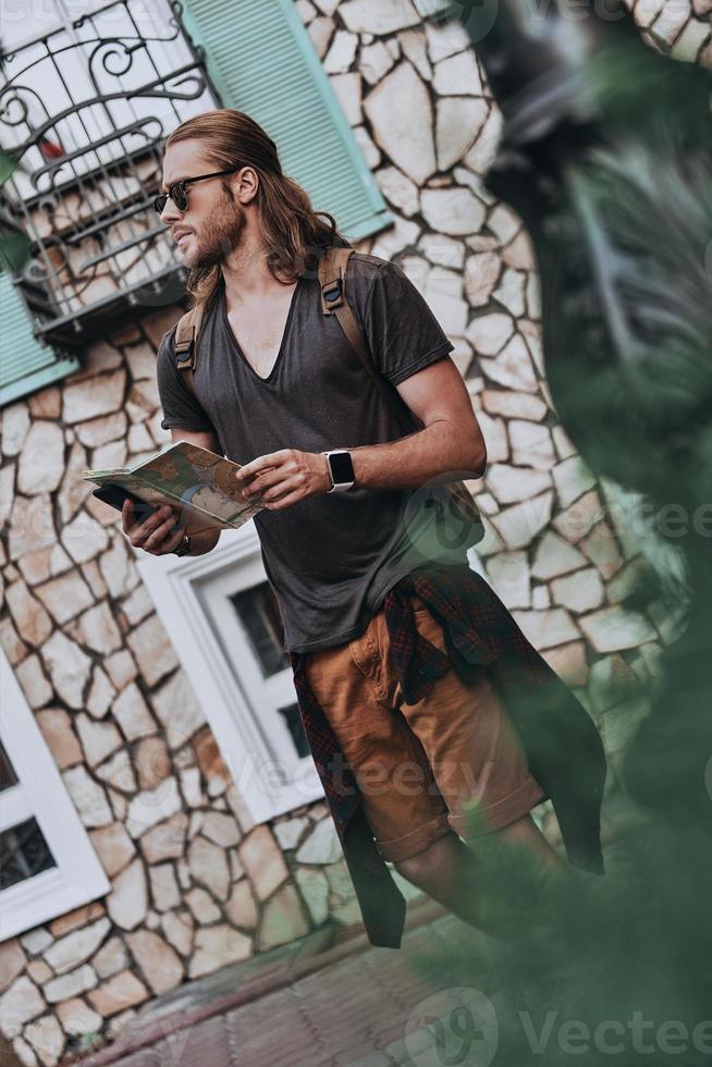 Modern tourist. Handsome young man in casual clothing holding map and looking away while standing outdoors photo