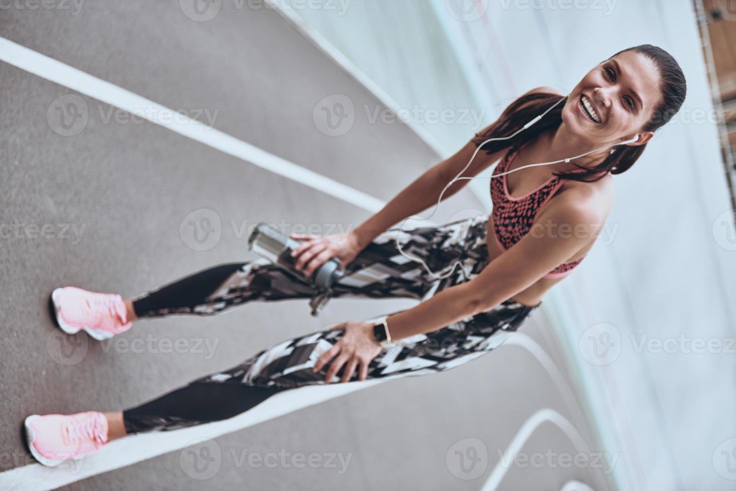 Everything is possible. Full length of young woman in sports clothing smiling while exercising outdoors photo