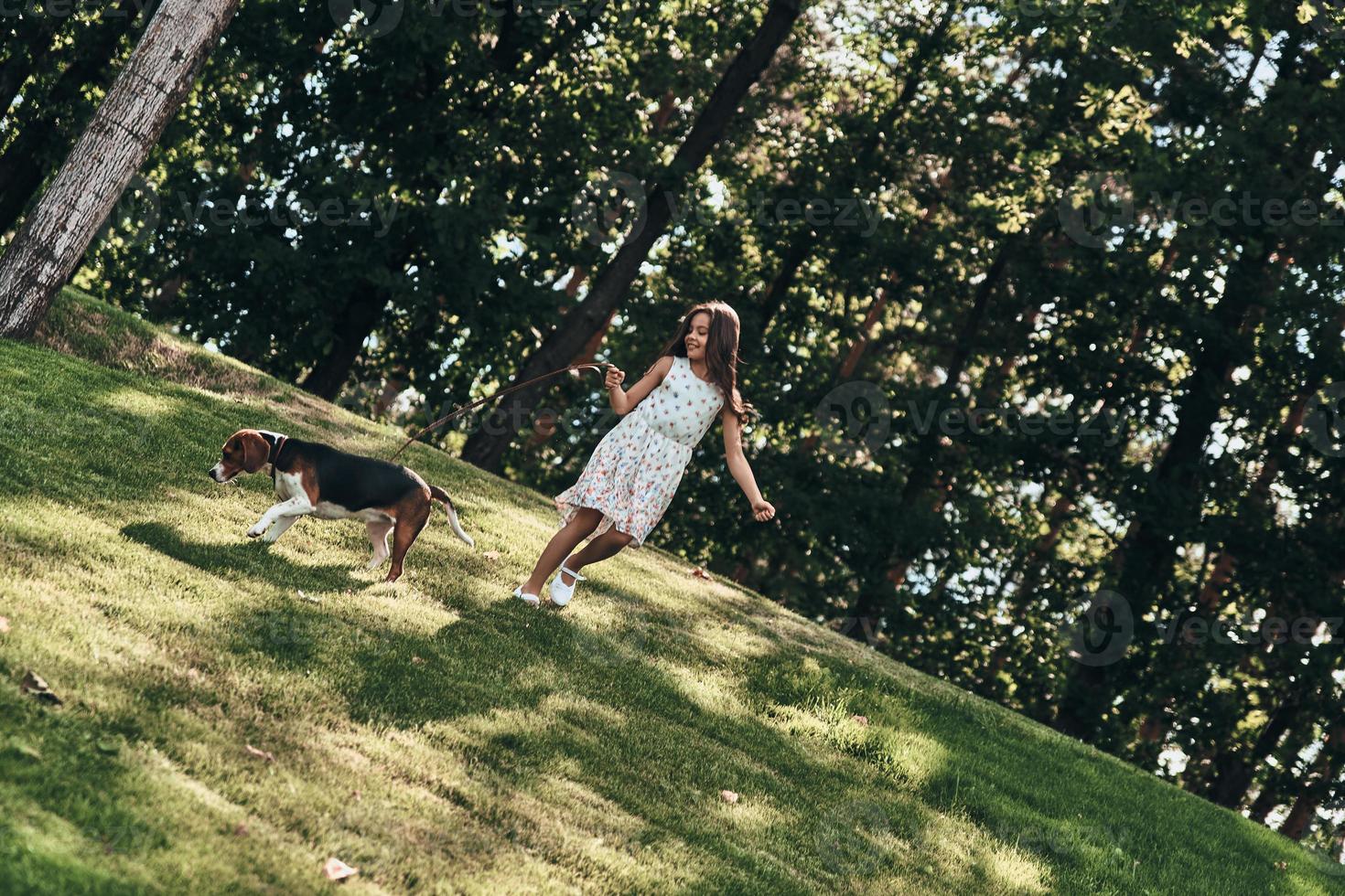 buscando aventuras juntos. toda la longitud de una linda niña jugando con su perro mientras corre al aire libre foto