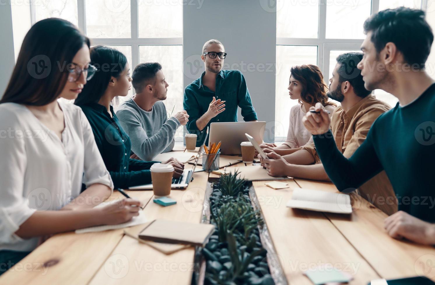 Discussing risky ideas. Group of young modern people in smart casual wear discussing something while working in the creative office photo