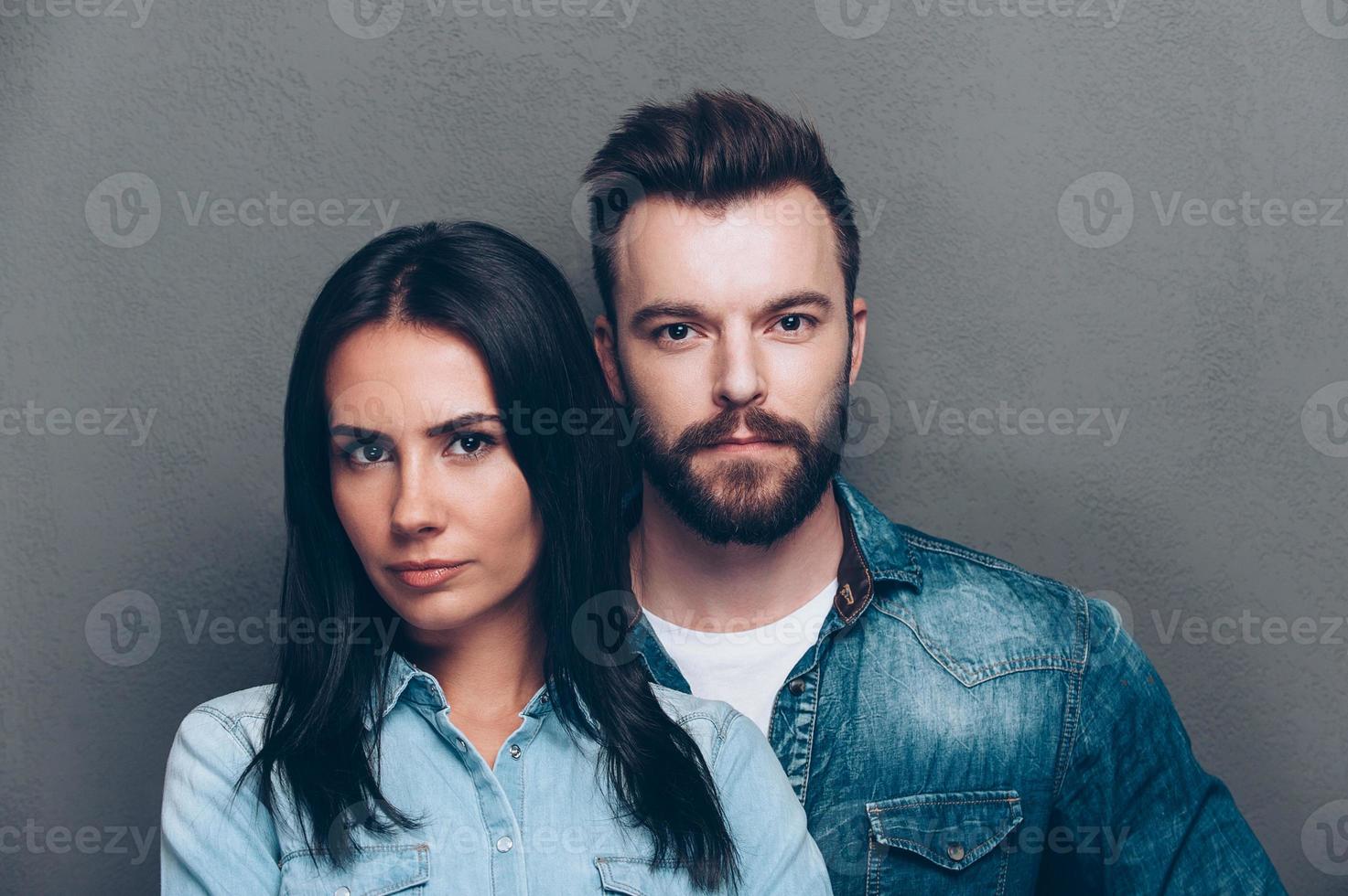 Beautiful couple. Portrait of beautiful young couple in jeans wear looking at camera while standing against grey background photo