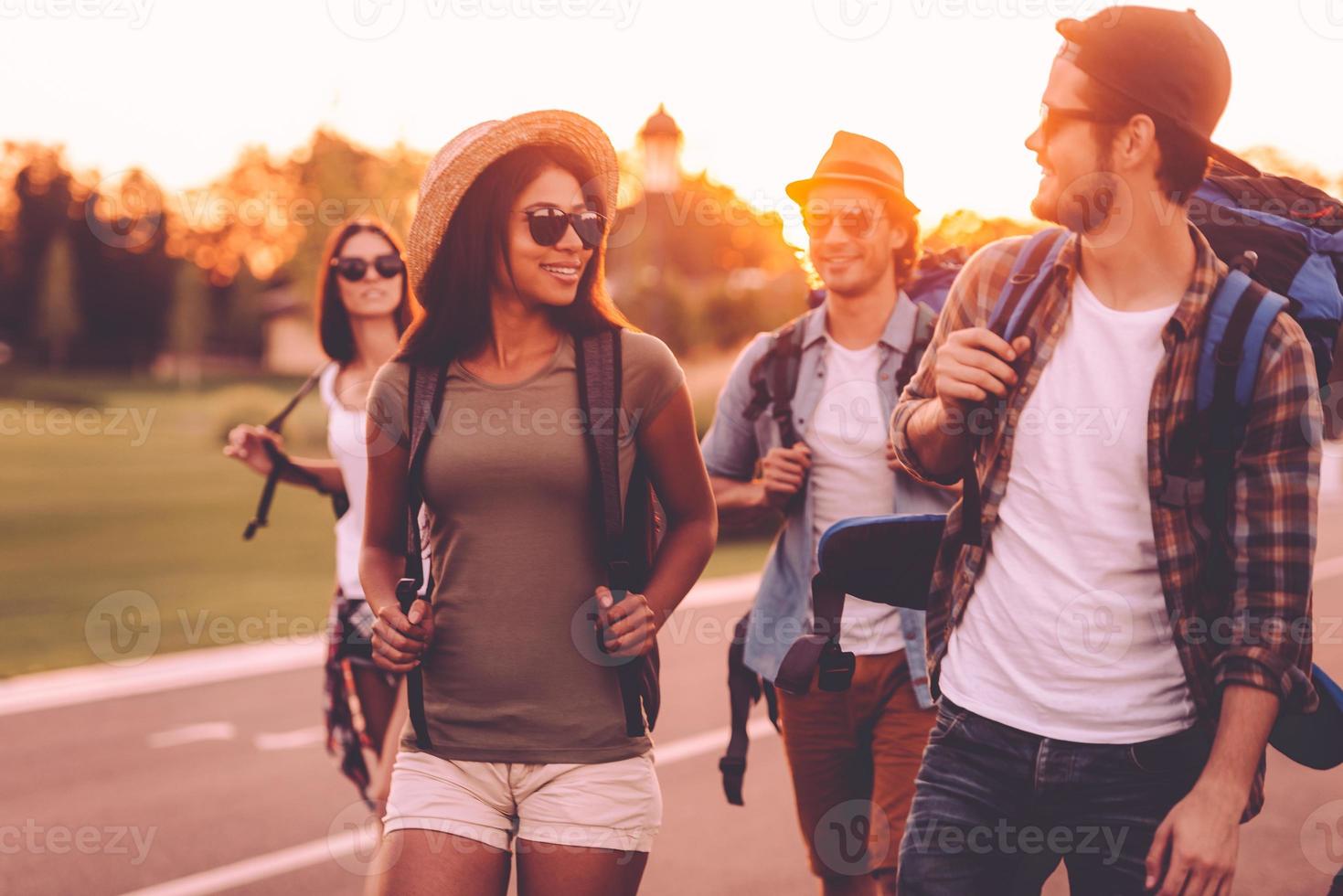 Having freedom to go anywhere. Group of young people with backpacks walking together by the road and looking happy photo