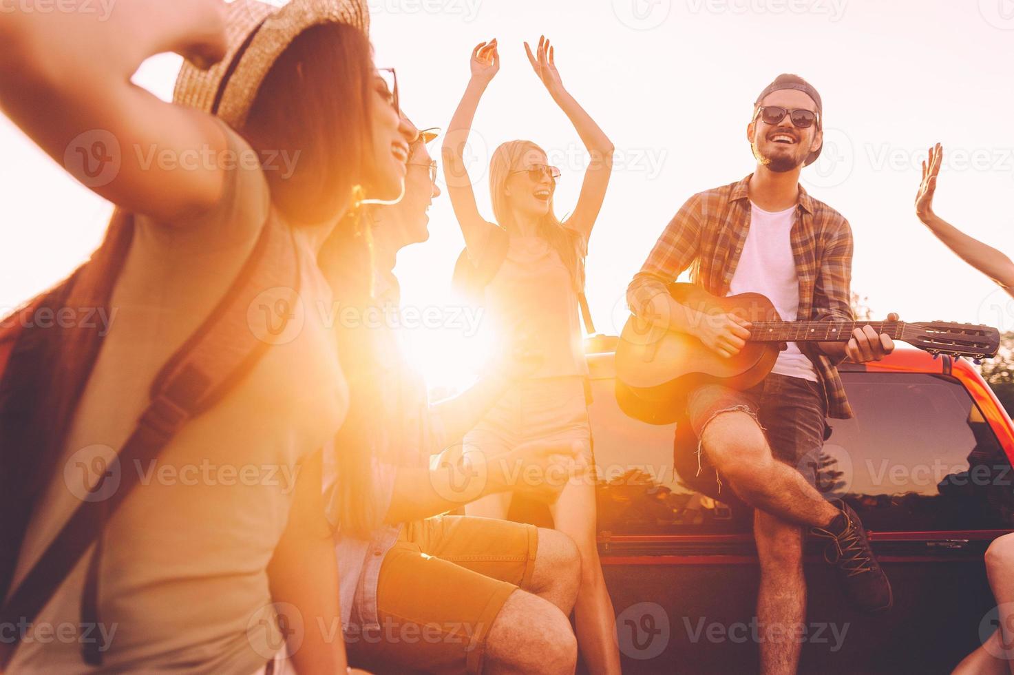 el mejor viaje por carretera jamás. grupo de jóvenes alegres bailando y tocando la guitarra mientras disfrutan juntos de su viaje por carretera en un camión de recogida foto