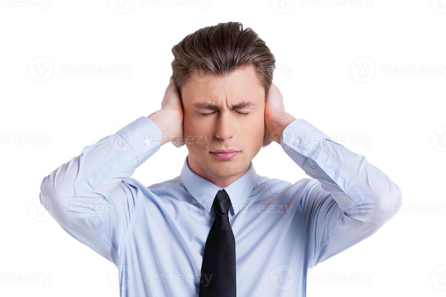 Sick and tired. Frustrated young man in shirt and tie covering ears with hands and keeping eyes closed while standing isolated on white photo