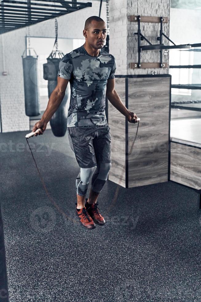Best cardio ever. Full length of young African man in sport clothing skipping rope while exercising in the gym photo