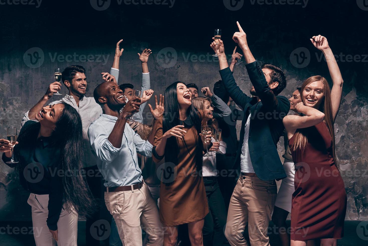 Enjoying amazing party. Group of beautiful young people dancing with champagne flutes and looking happy photo