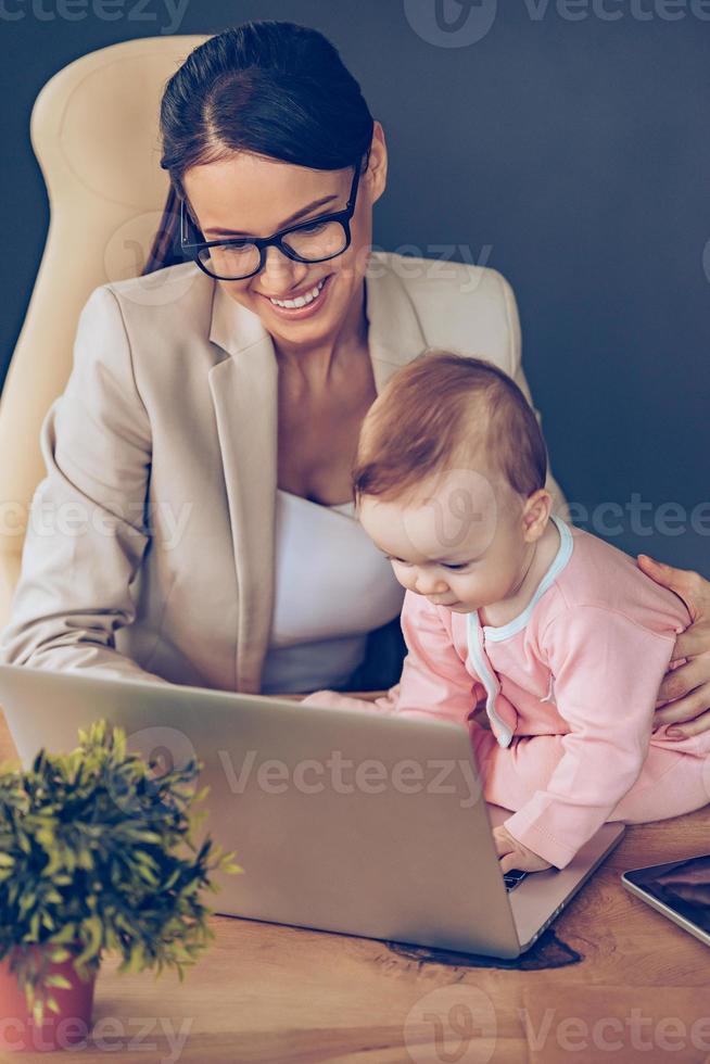 I can help you Top view of little baby girl using laptop while sitting on office desk with her mother in office photo