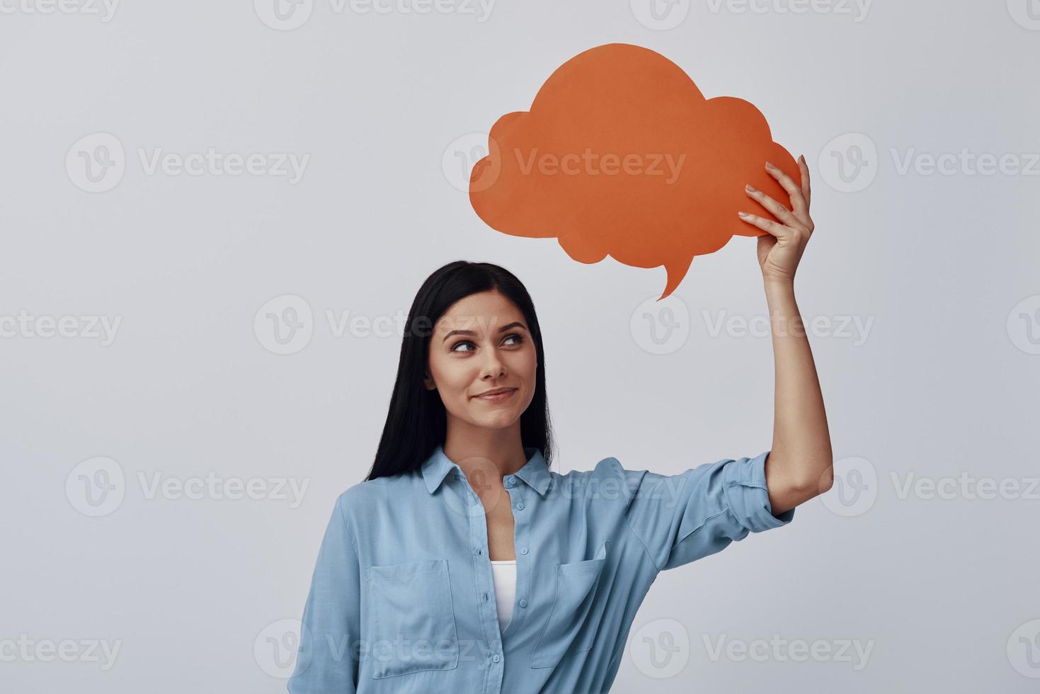 Thoughtful young woman smiling while standing against grey background photo