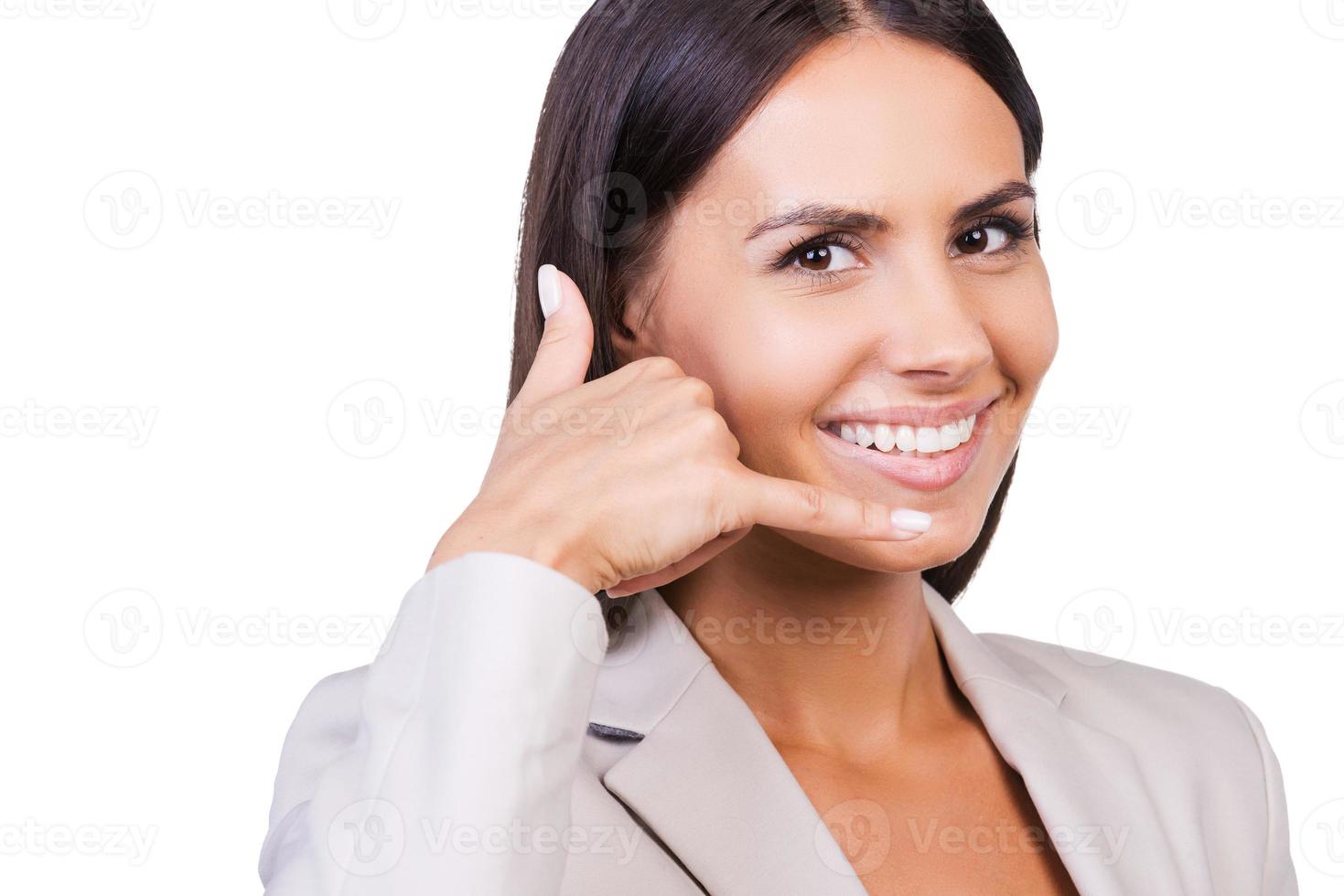 Waiting for your call Happy young businesswoman in suit gesturing mobile phone and smiling while standing against white background photo