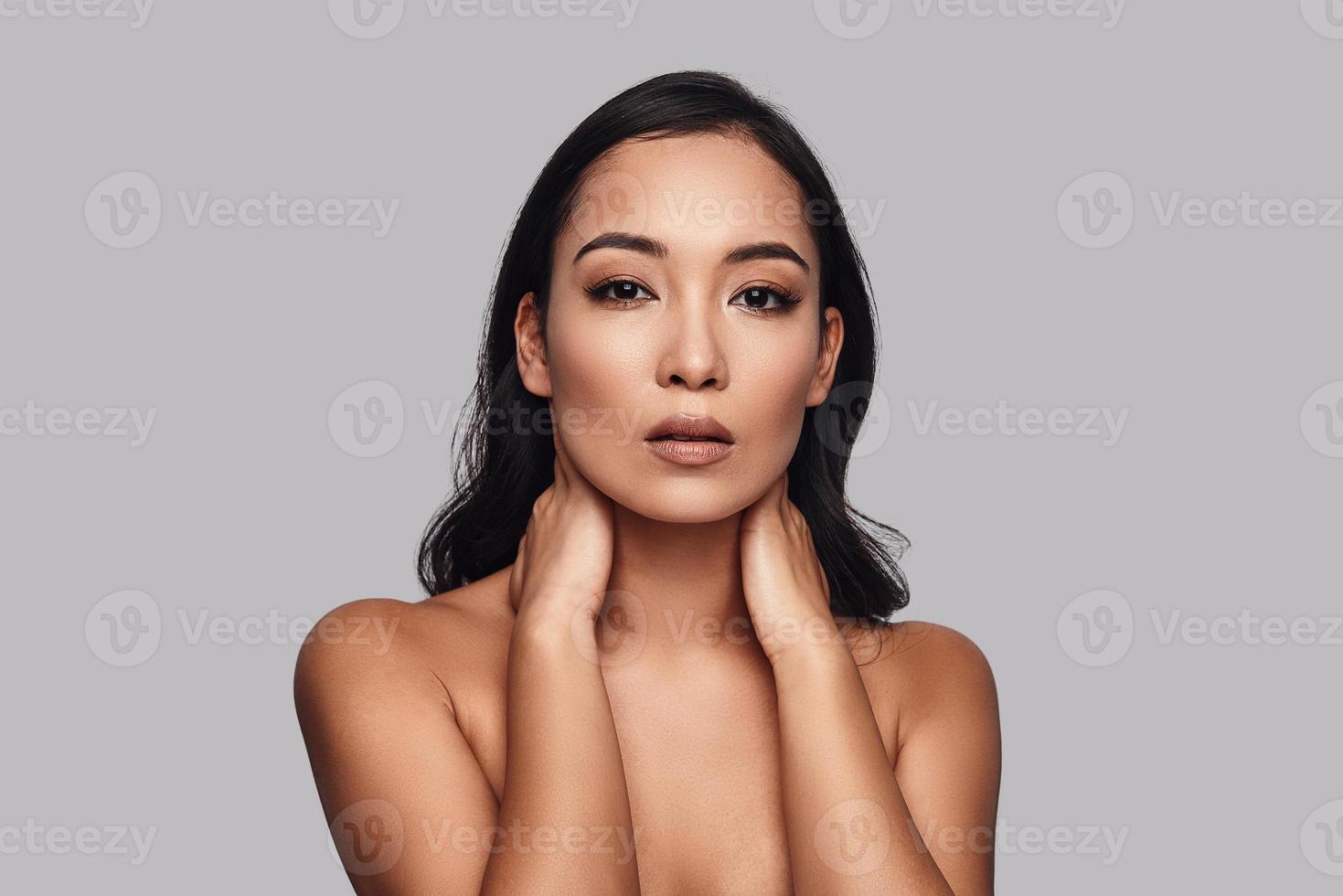 Supremely sensual. Beautiful young woman touching her shoulder with hand  while standing against grey background 13517833 Stock Photo at Vecteezy